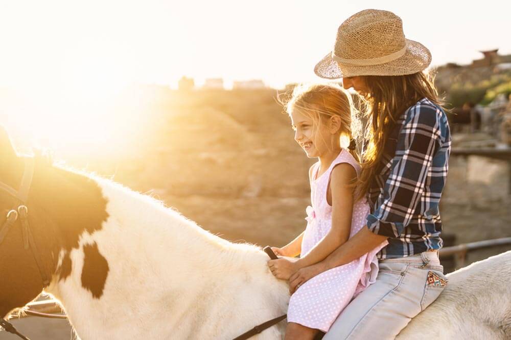 Happy mother and daughter having fun riding horse